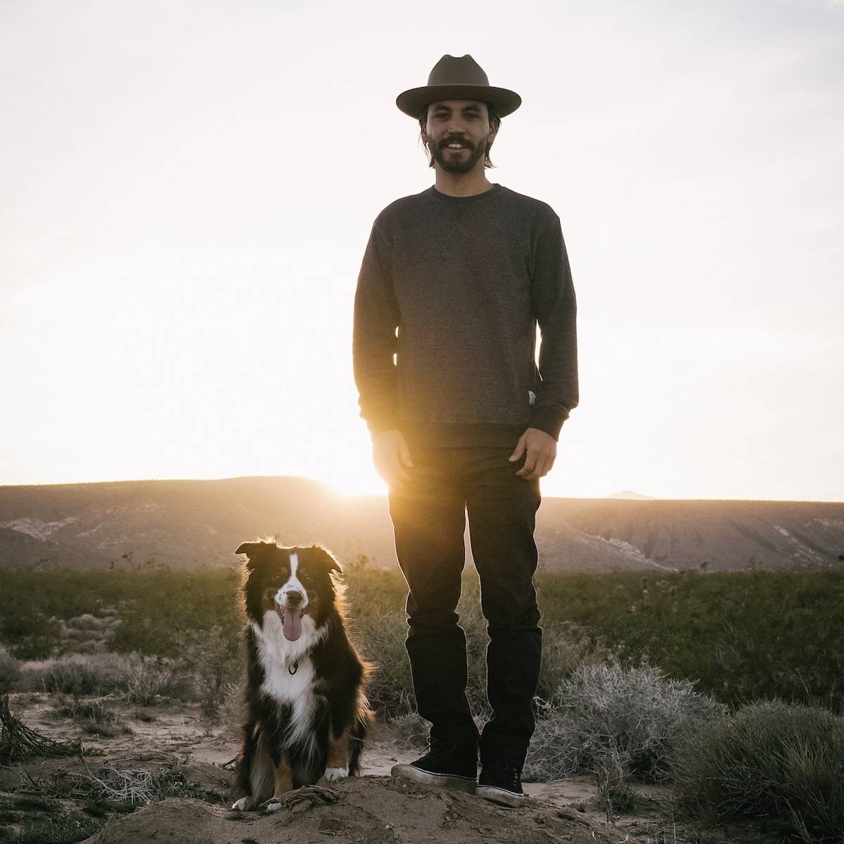 Samson Hatae and his Australian shepherd dog Jax in front of a sunset