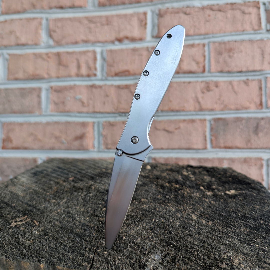 A folding knife resting on a wooden surface against a brick wall.