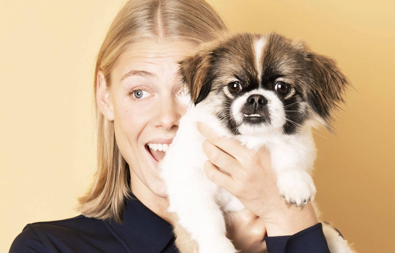 Femme souriante tenant un petit chien brun et blanc. Elle a répondu au questionnaire sur les allergies de klarify et contrôle ses symptômes