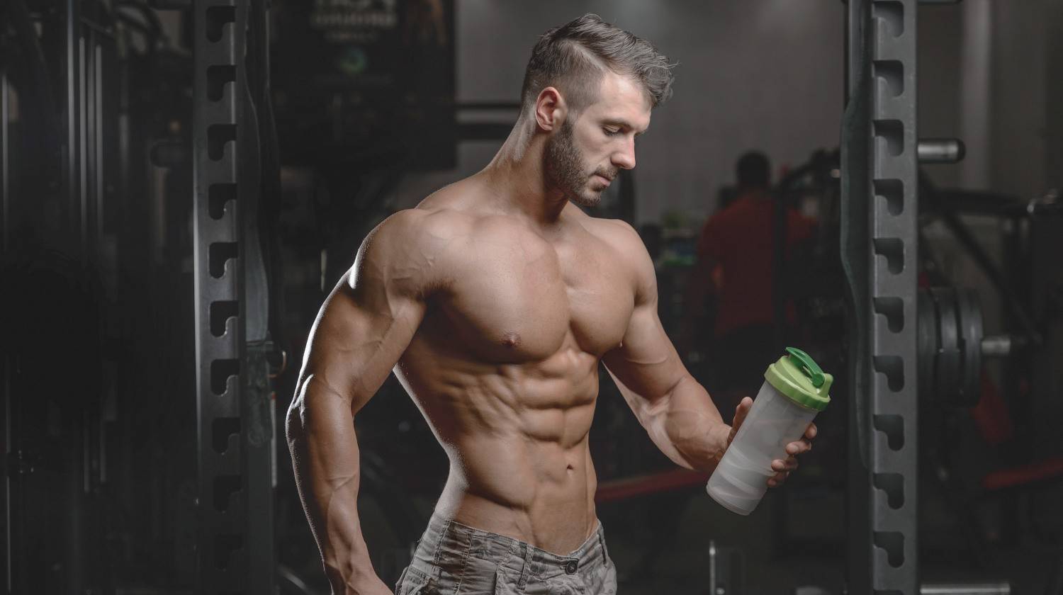 Handsome athletic fitness man holding a shaker and posing gym | The Essential and Optimal Drink for Bodybuilders | bodybuilding drinks | water for bodybuilders | Featured