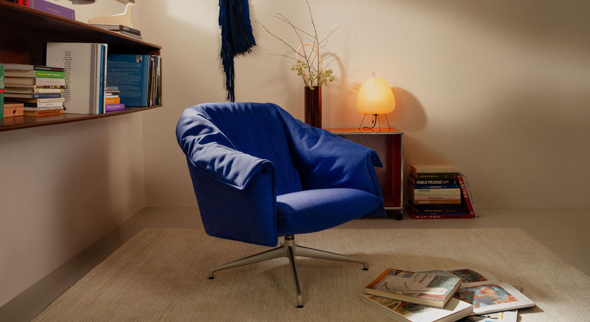 A blue bascule chair in a cozy interior with a lamp and books.