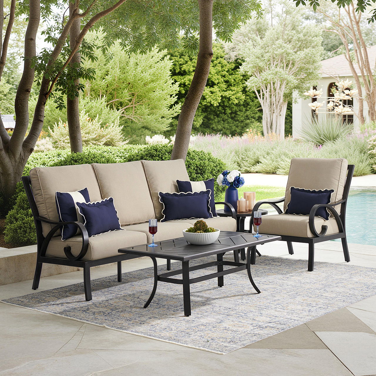Outdoor seating area with cushions by a pool surrounded by greenery.