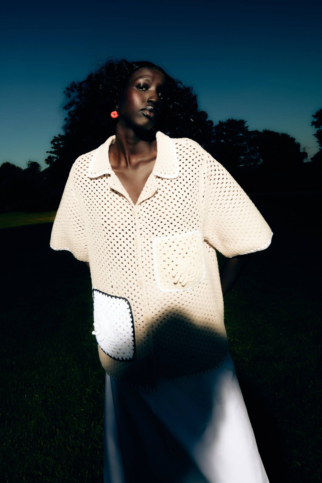 Model wearing a light, perforated shirt, posing against a dark background.