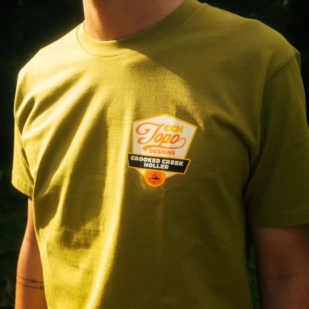 Person wearing an olive green t-shirt with a logo on the chest.