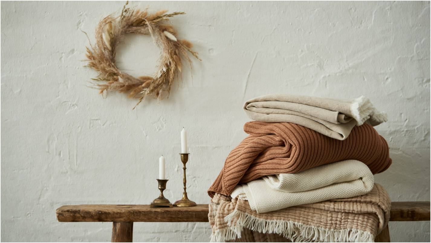 Pile of warm coloured blankets against a cream background.  Earthy tones.