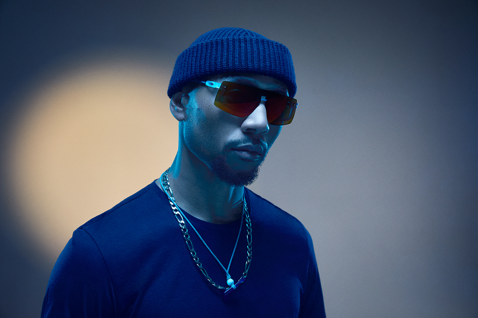 A person wearing sunglasses and a beanie in a blue-lit setting.