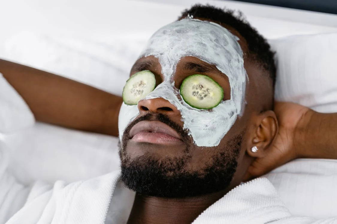 a man relaxing with a cream on his face and sliced cucumber on his eyes