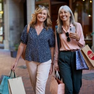 Two women smiling while walking with shopping bags.