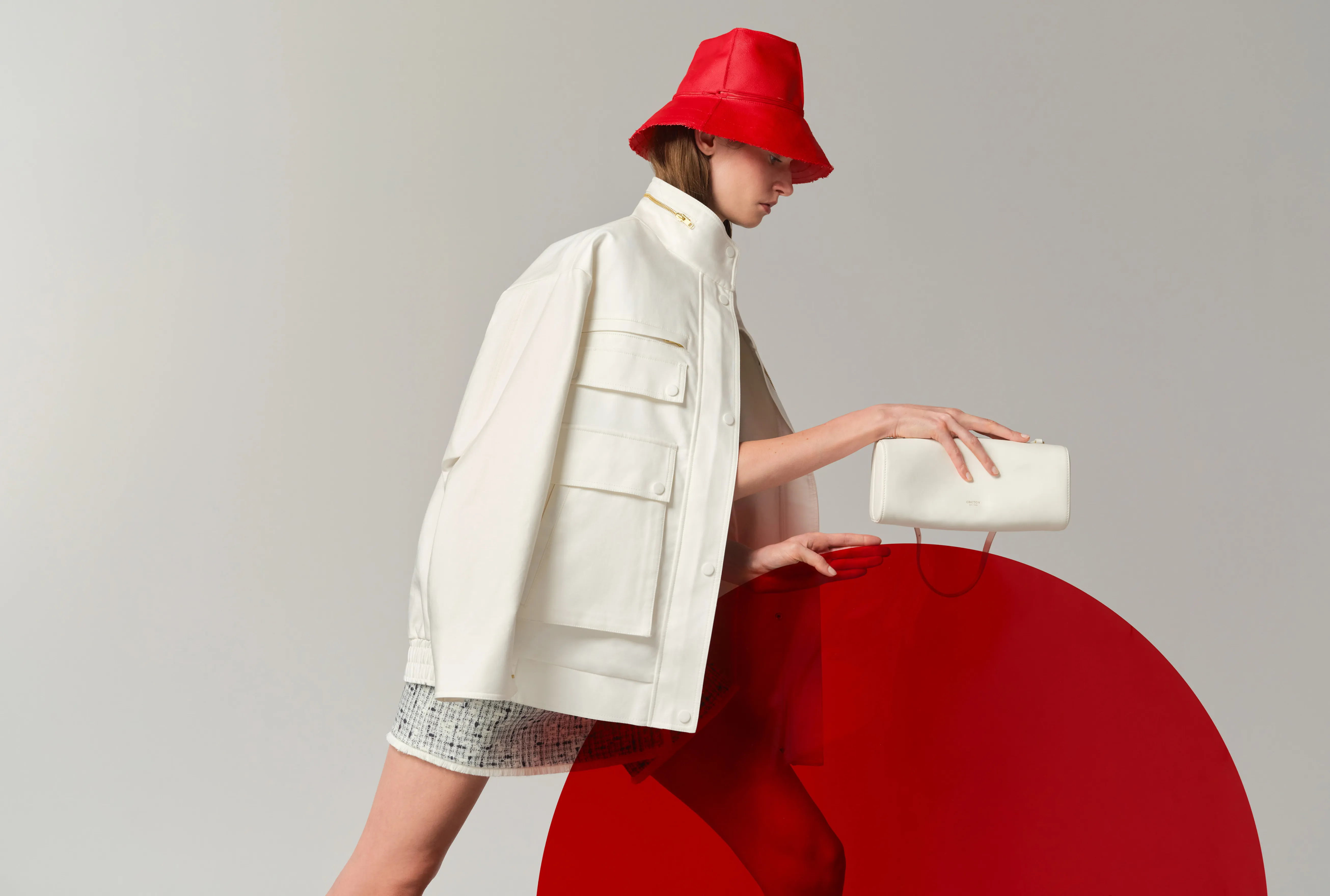 A model in a white jacket and red hat poses with a circular red prop.