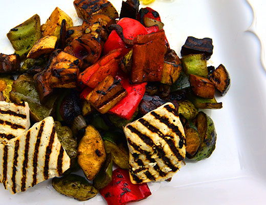 Grilled vegetables and sliced cheese on a white plate.