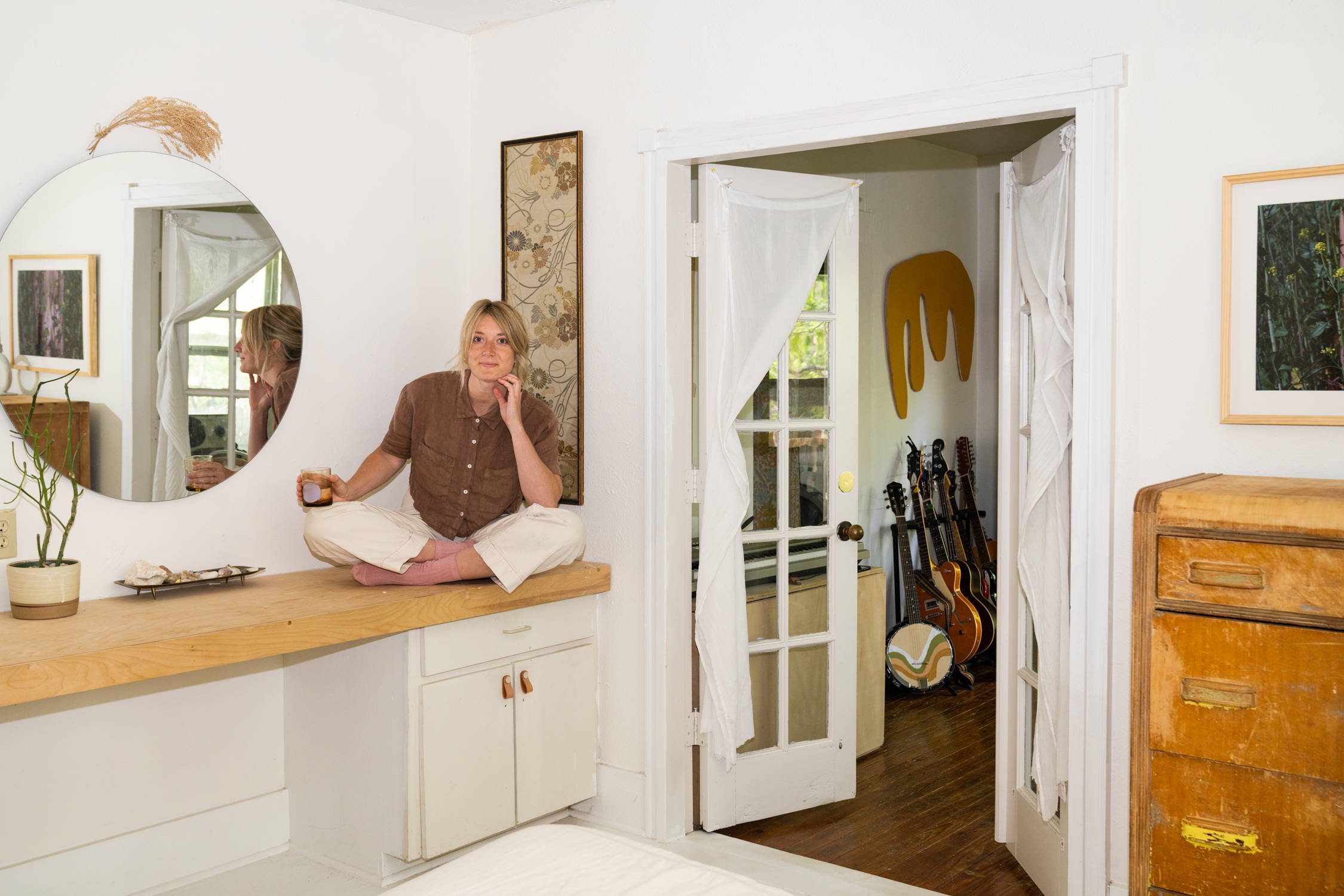 O’Connor in bedroom with circle mirror, wood platform vanity and breezy doorway
