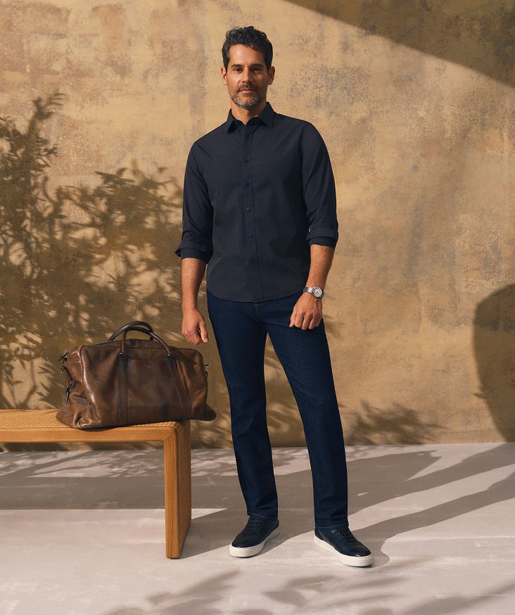 A man in a dark shirt and pants stands beside a bag.