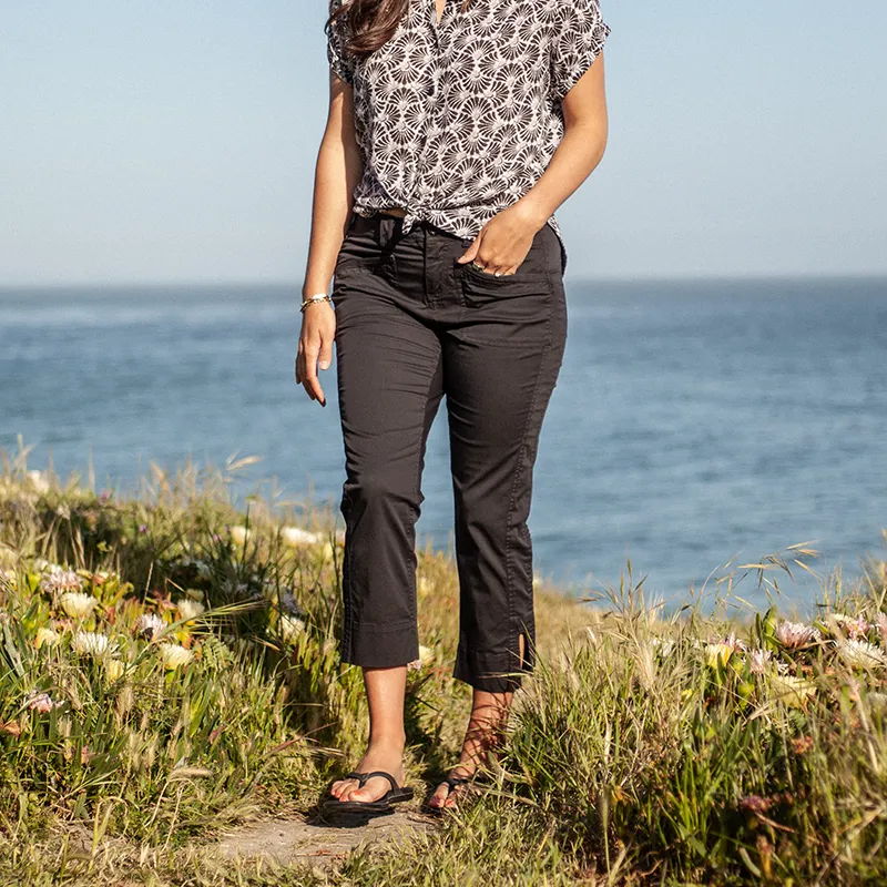 Woman in casual attire standing near the ocean with flowers in the foreground.