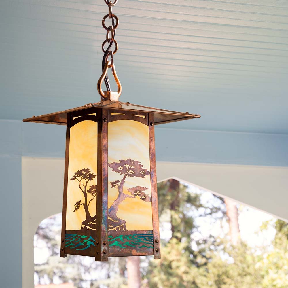 A chain pendant lantern with tree artwork in a raw copper finish. It's hanging from a blue wood ceiling.