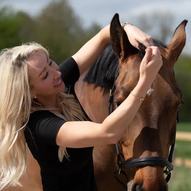 Woman using BEAUTIFY OIL on her horse in a sunny outdoor setting.