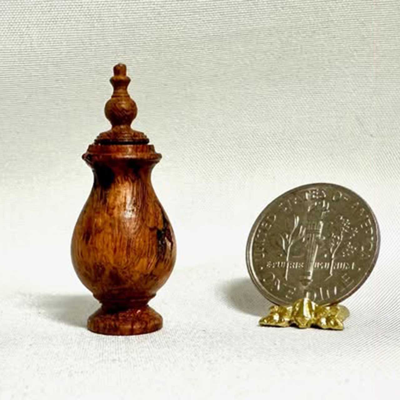 A small wooden urn next to a quarter and gold-colored objects.