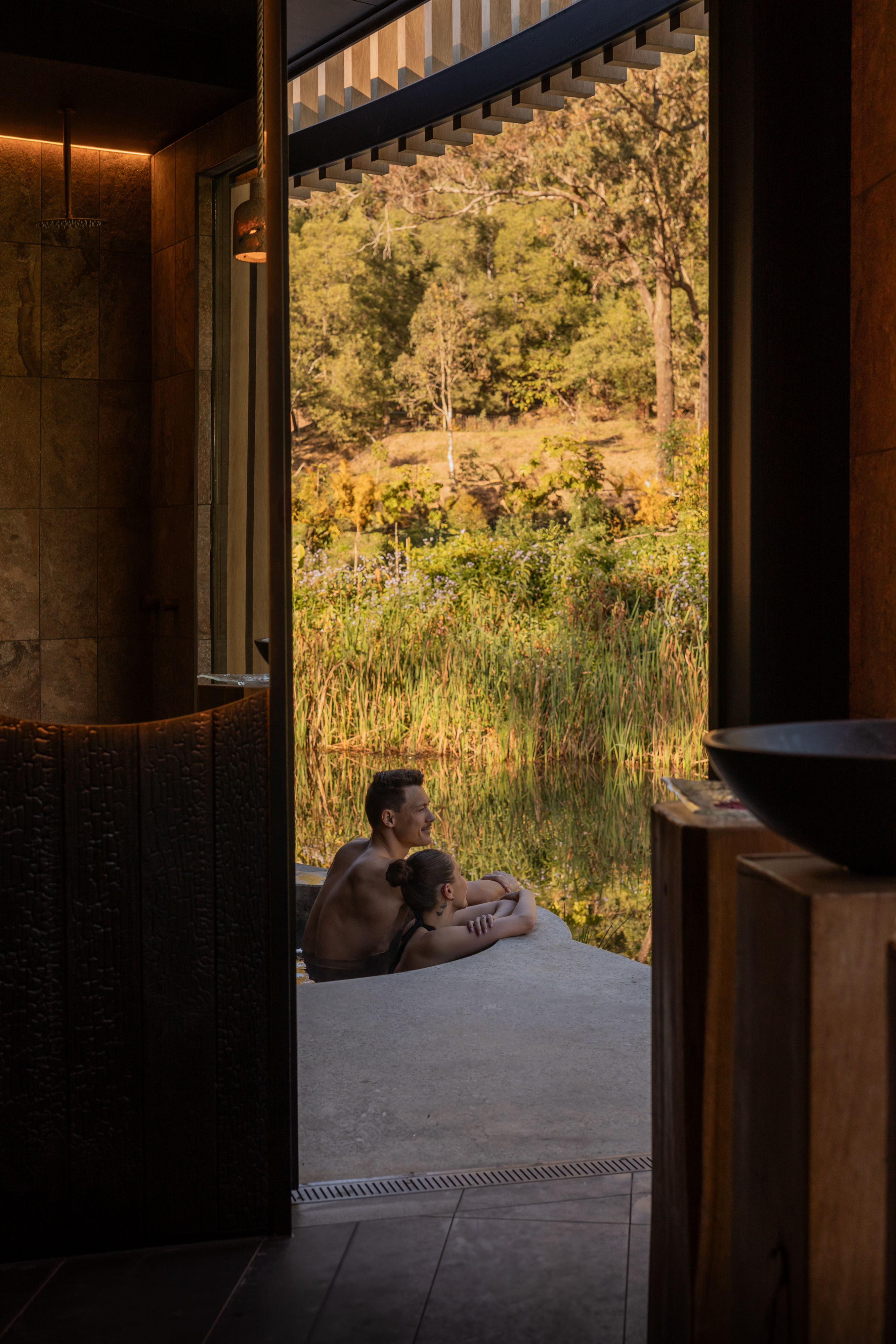 A couple in a spa overlooking a lake and trees