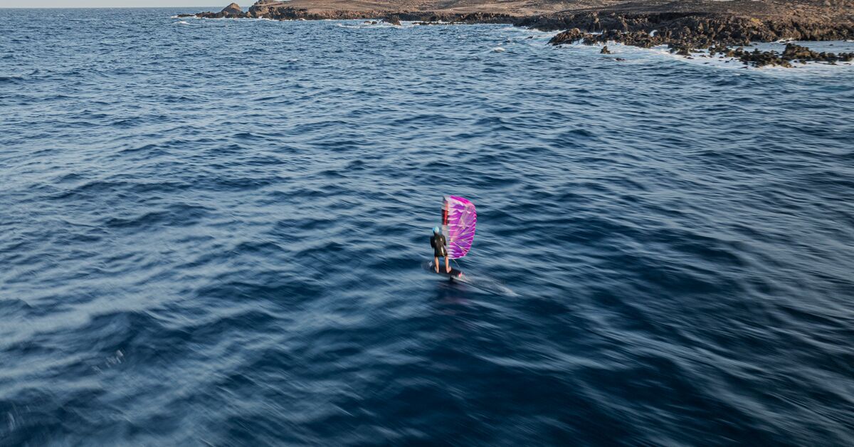 Person with a pink paarwing on calm water near rocky shore.