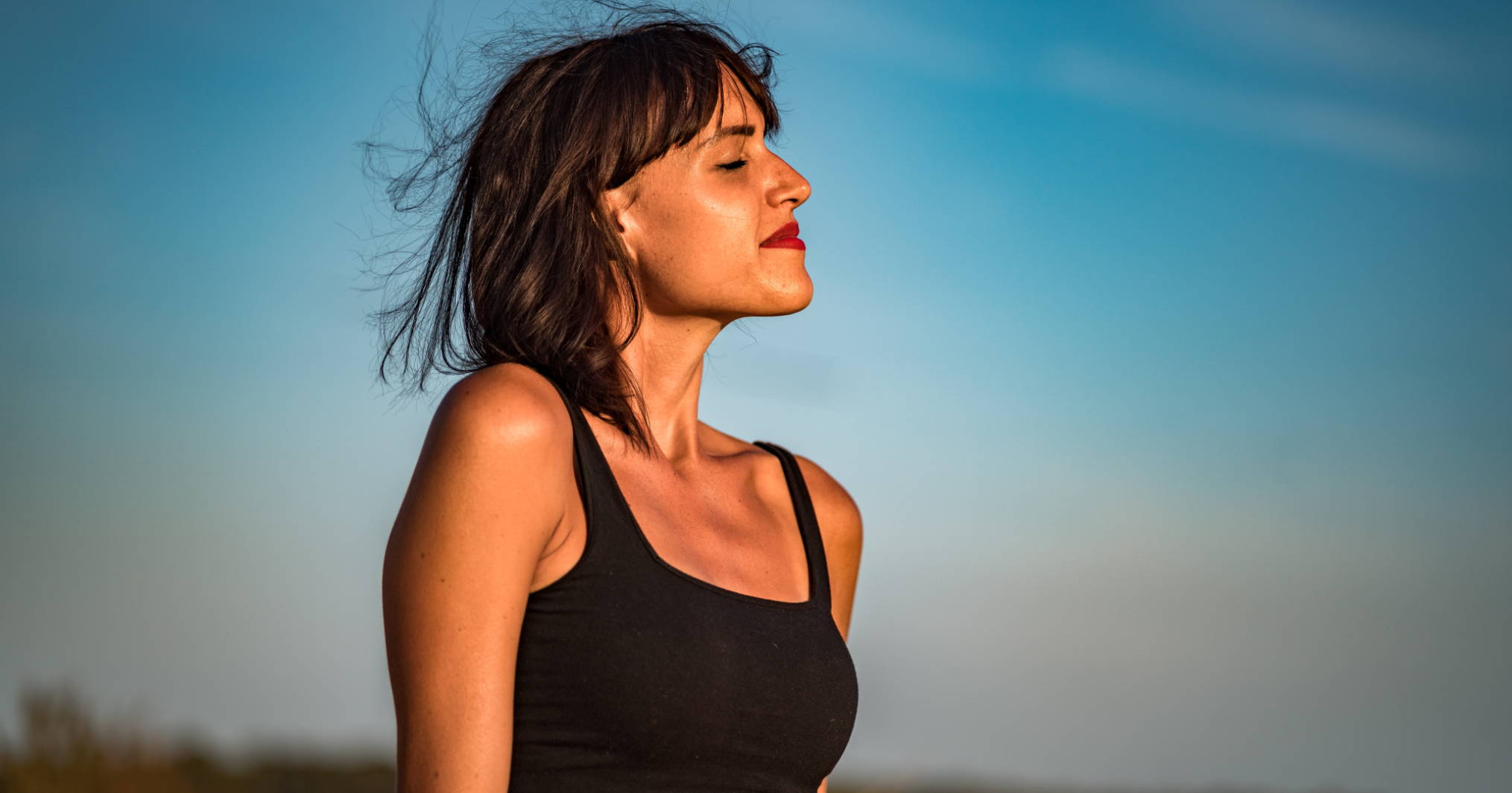 A woman smiling in the sun and closing her eyes wear form-fitting shapewear to avoid bra showing through shirt.