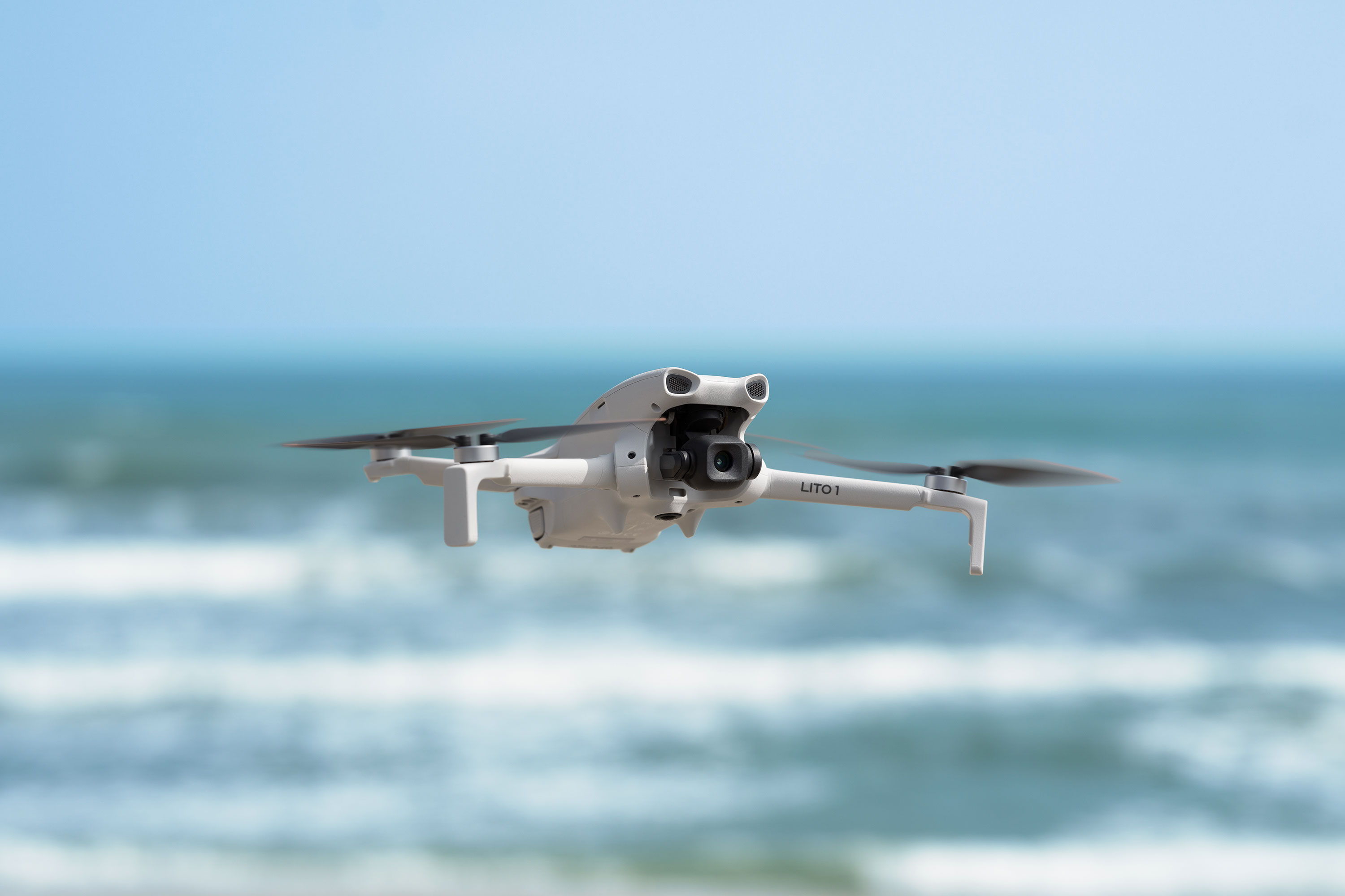 A DJI Lito 1 drone flying over the ocean with waves in the background.