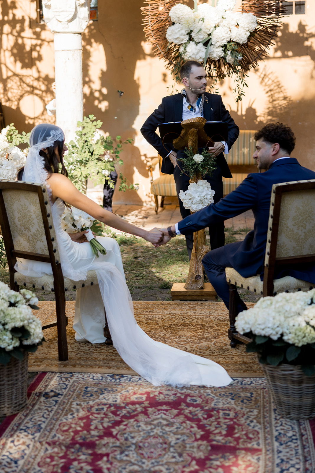 A couple holding hands during a wedding ceremony with floral decorations.