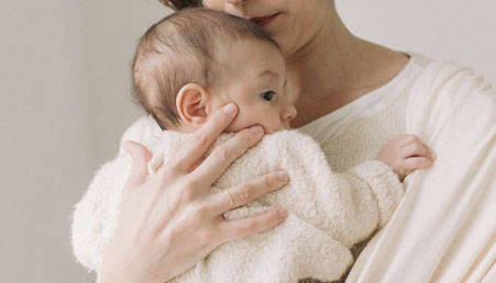 mother-placing-awake-newborn-baby-in-cream-boba-wrap