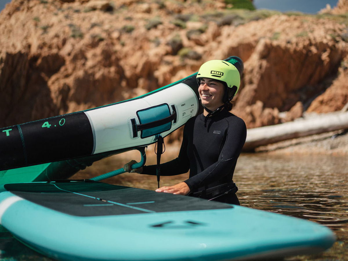 Person smiling while holding a paddleboard in a serene water setting.