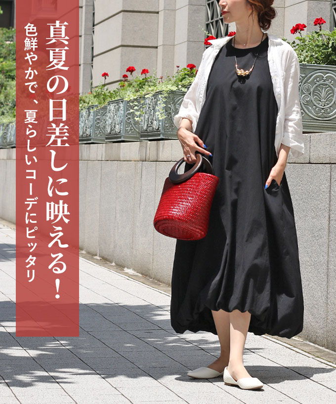A woman in a black dress holding a red bag outdoors.