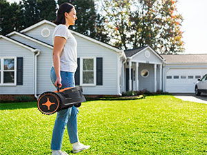 Person carrying a robot mower on a lawn in front of a house.