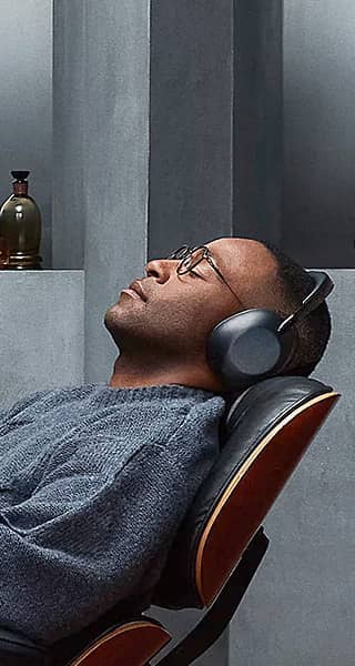 A person wearing over-ear headphones relaxing in a chair with a thoughtful expression.