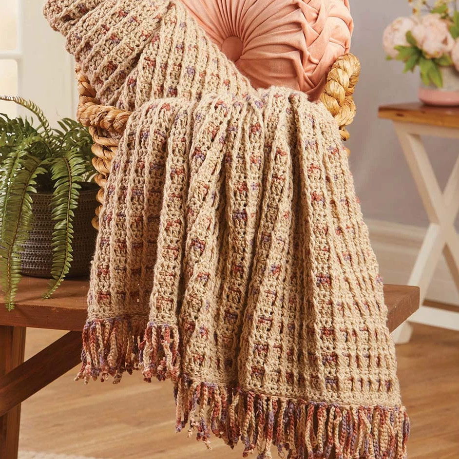 A knitted blanket draped over a chair with a decorative pillow.