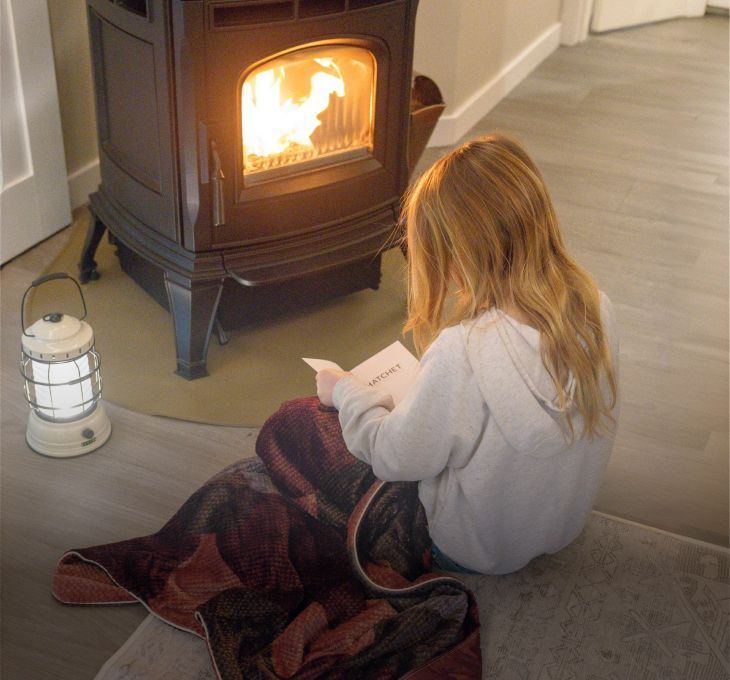 Child reading by a warm fire, wrapped in a blanket.