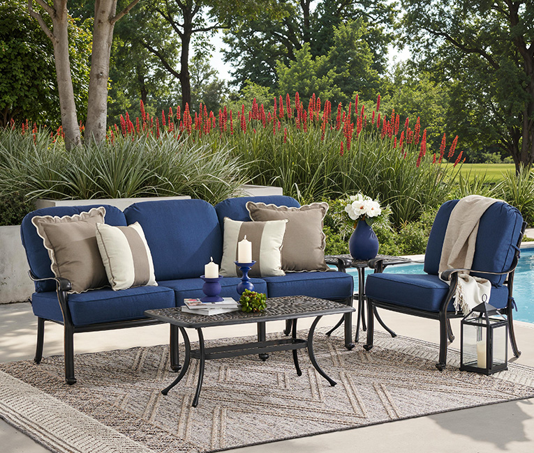 Outdoor seating area with blue cushions, decorative pillows, and a coffee table.