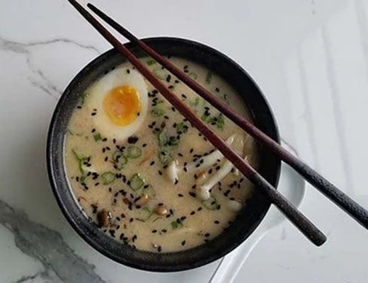 Bowl of ramen with egg, green onions, and chopsticks.