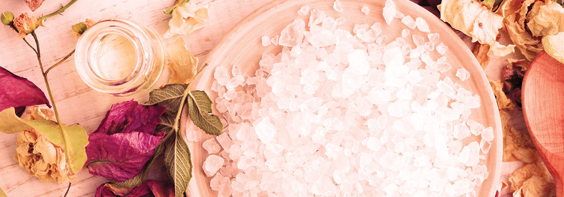 Bowl of ice surrounded by flowers and a glass.