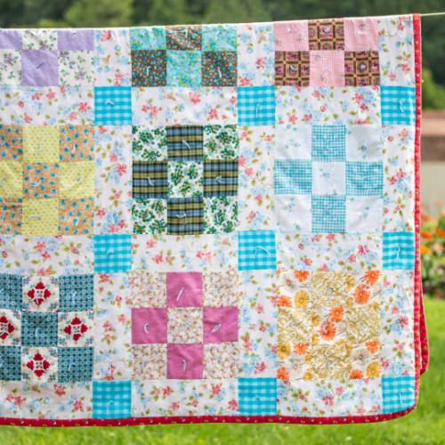 a quilt hanging with squares in the garden
