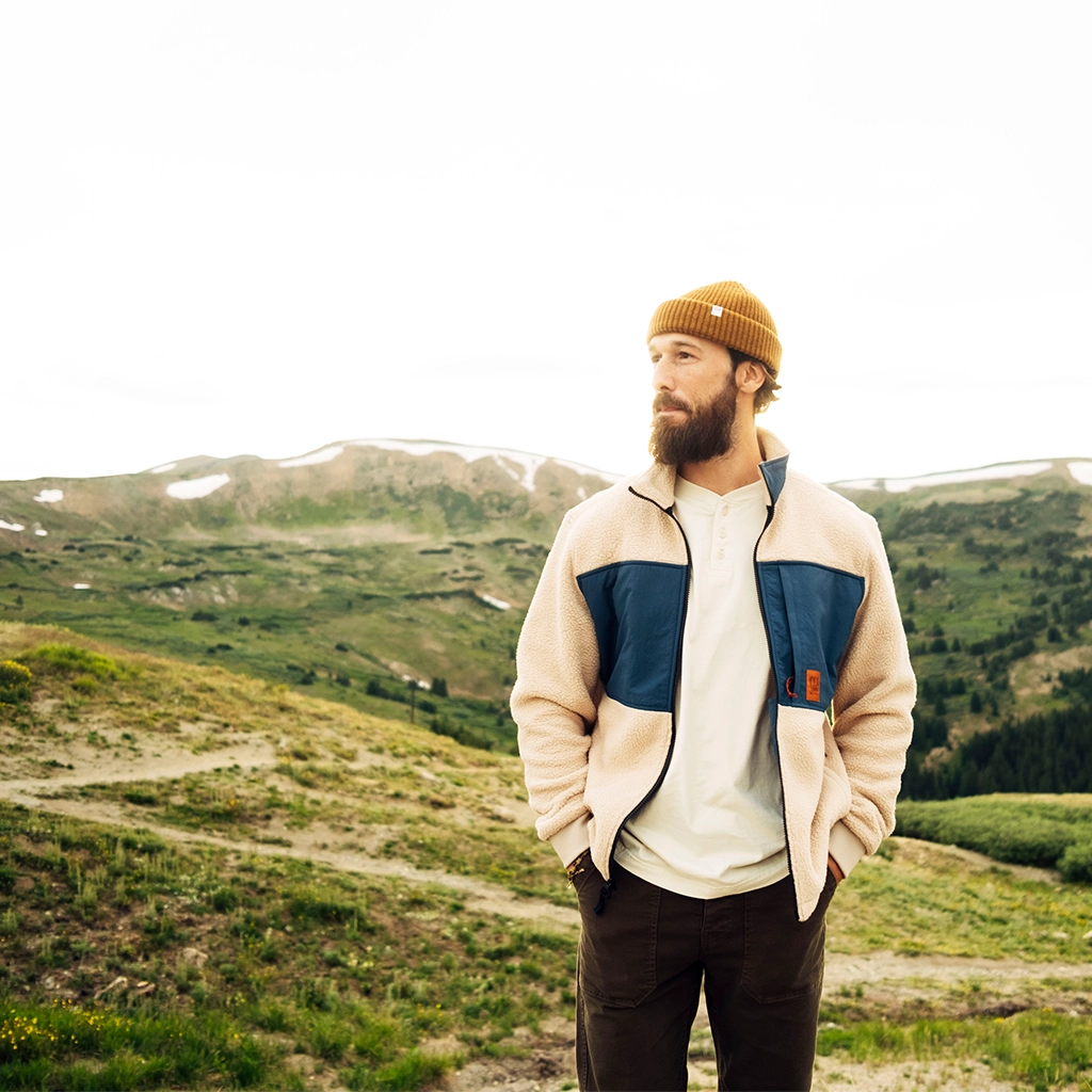 Person in a jacket and beanie standing in a mountainous landscape.