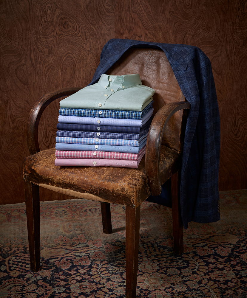 A stack of folded shirts on a chair with a jacket draped over it.