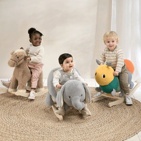 Three children riding plush animal toys on a rug.