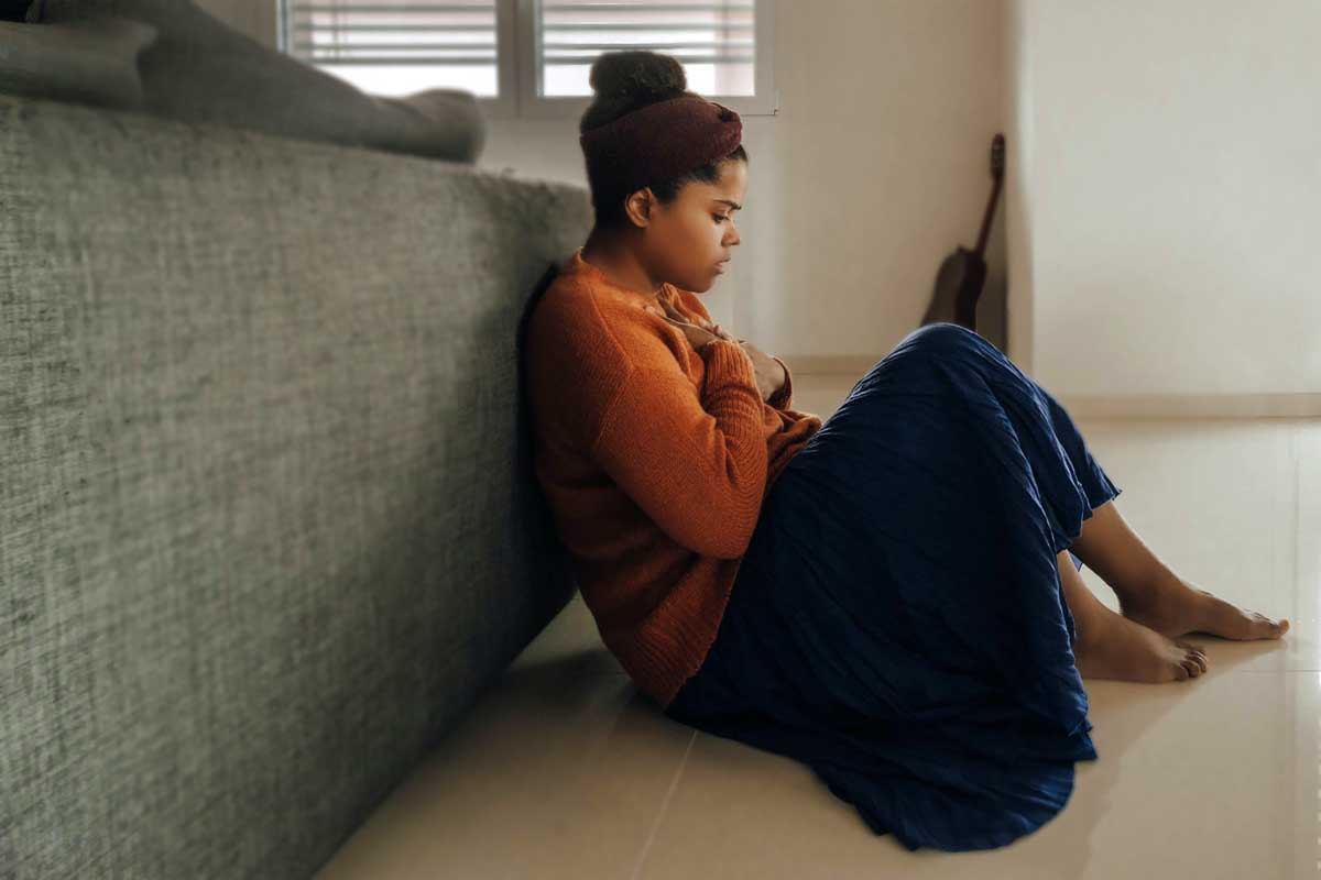 A woman sitting on the floor holding her chest, looking anxious