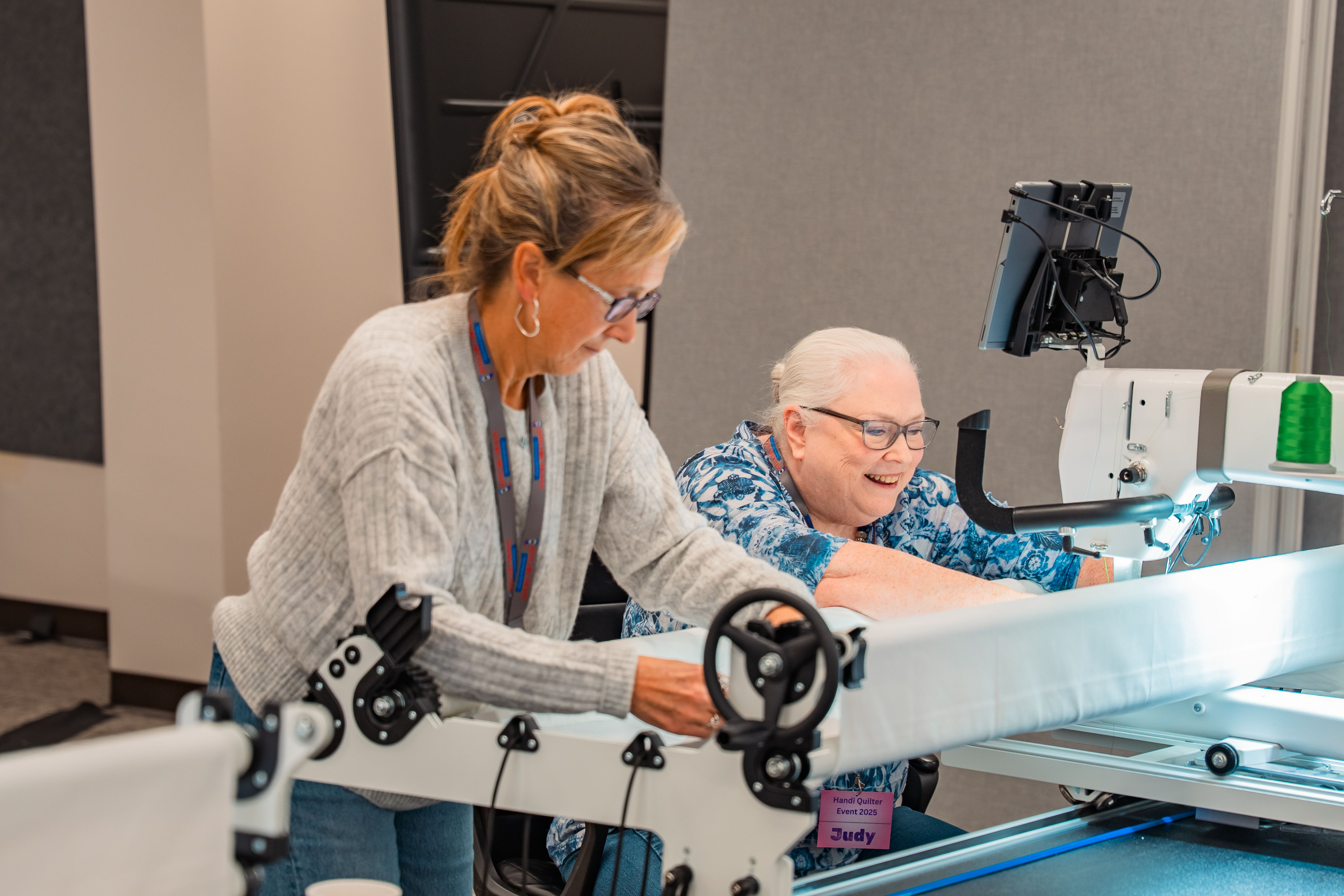 Two women working together on a sewing machine in a bright room.