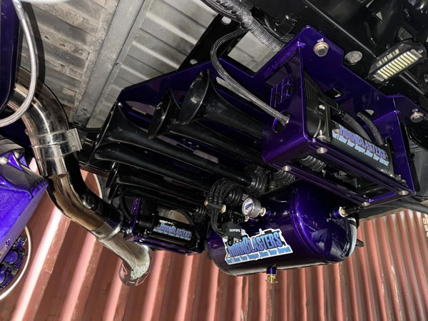 Undercarriage view of custom HornBlasters train horn kit with black trumpets, glossy metallic purple air tank, and purple mounting brackets