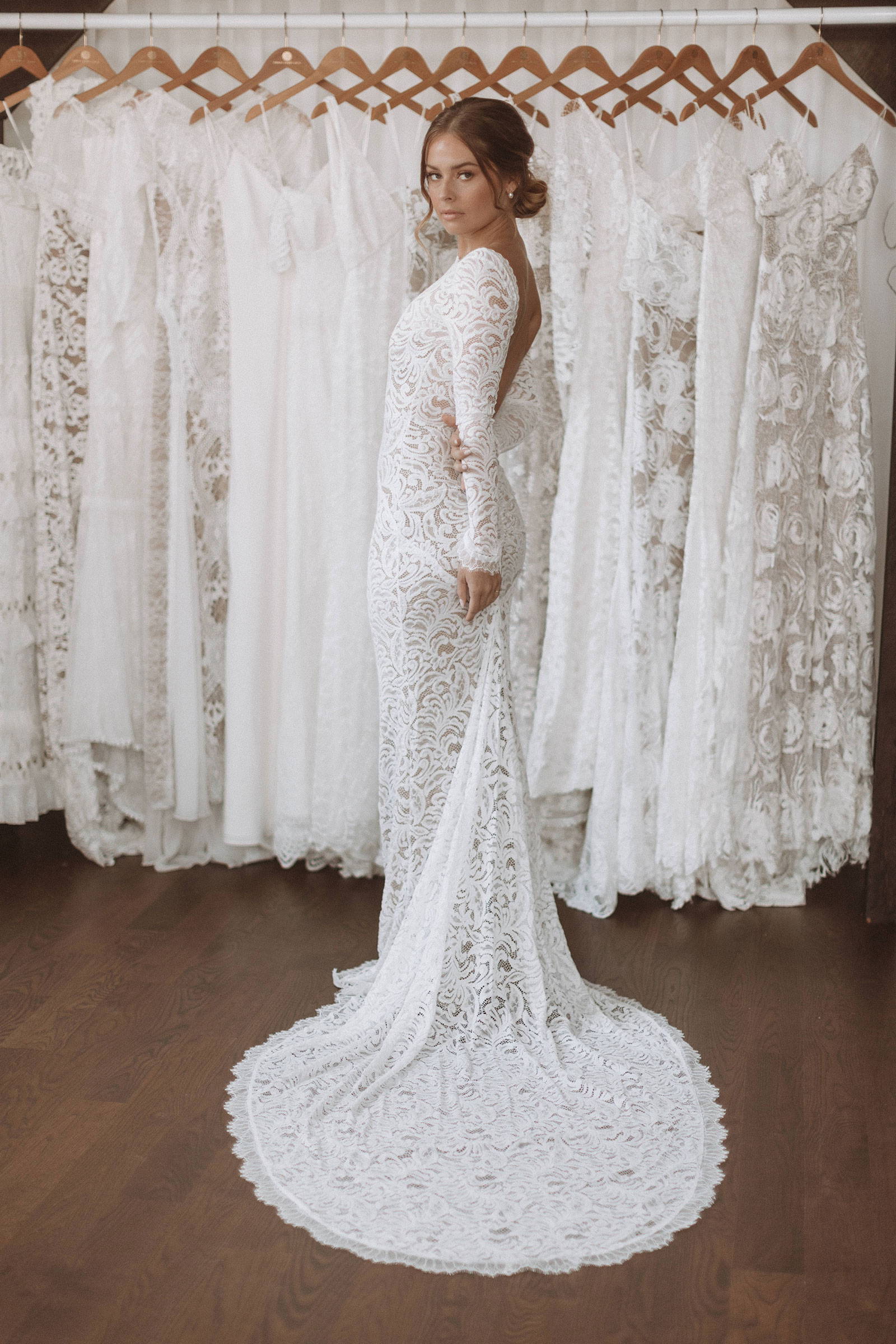 Women wearing the Grace Loves Lace Orla gown with backdrop of Grace Loves Lace hanging gowns