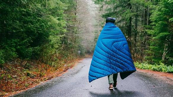 Man wrapped in Rumpl blanket walking in forest