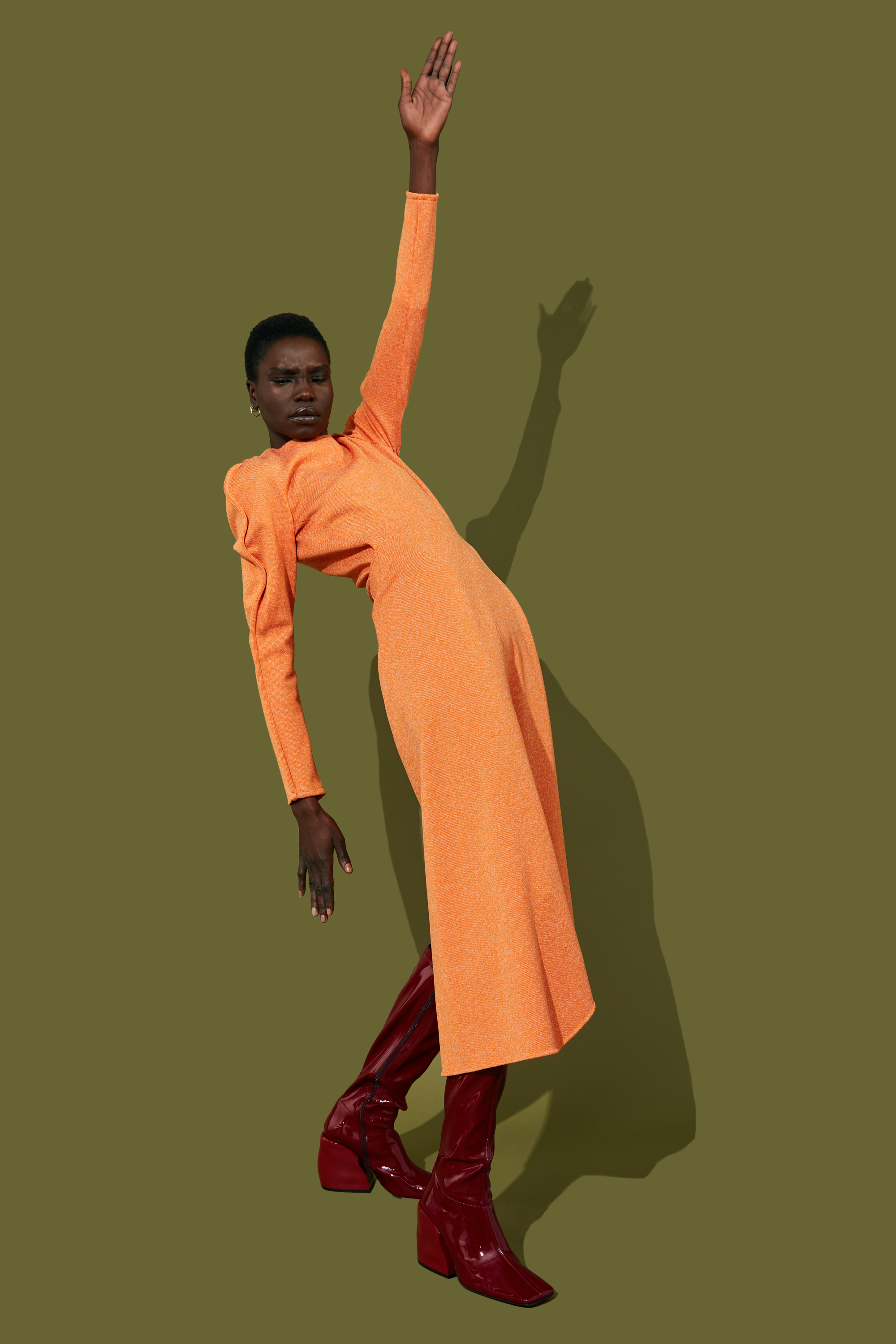A model in an orange dress poses against a green background.