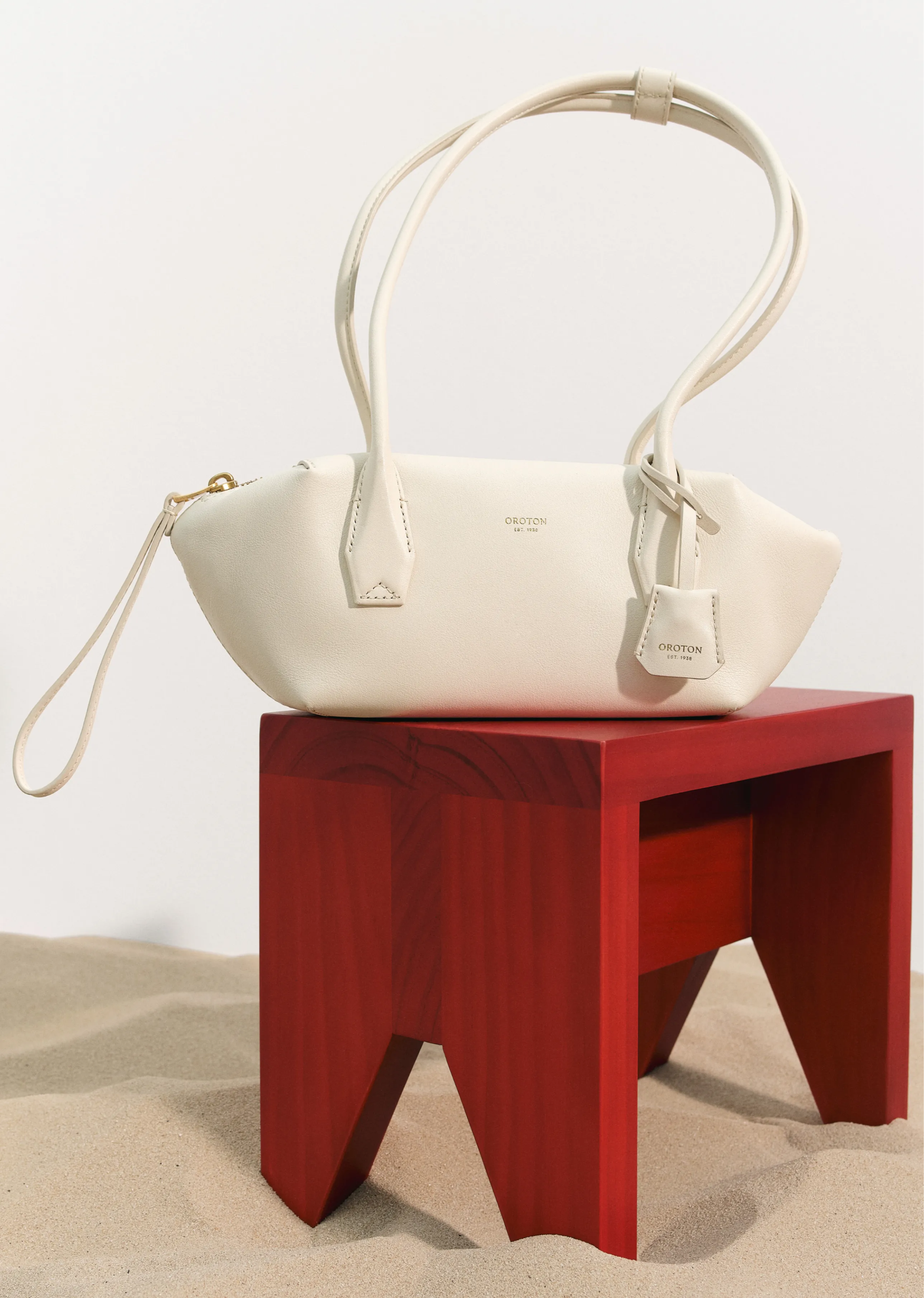 A white handbag on a red wooden stool in a sandy setting.