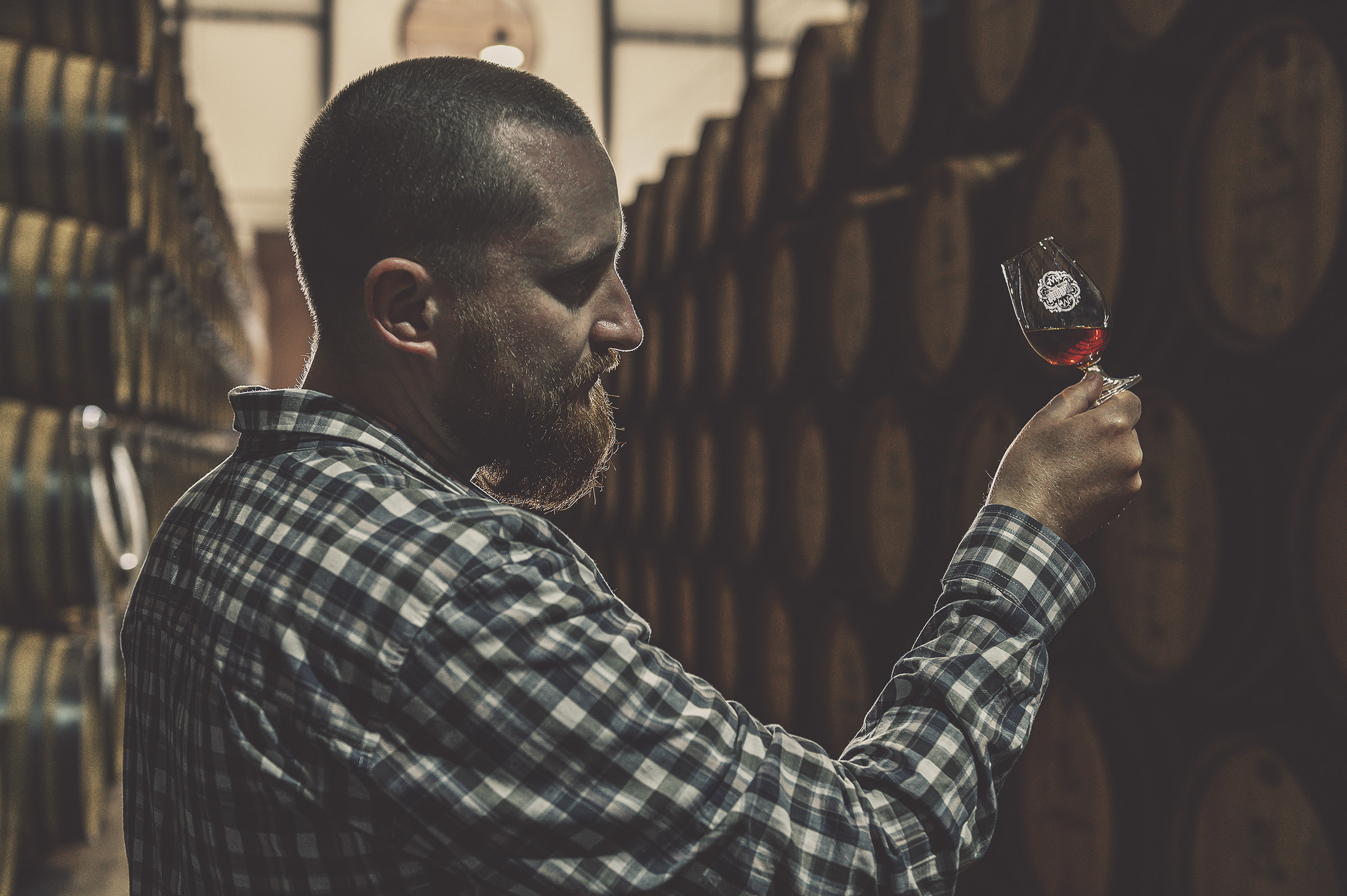 Man inspecting wine in a barrel cellar with a glass.