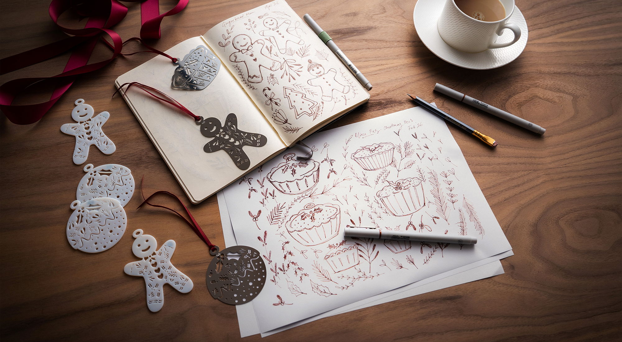A cozy workspace with sketches of Christmas decorations, pens, and a cup of coffee.
