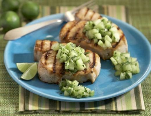 Grilled fish with cucumber salsa on a blue plate with lime wedges.