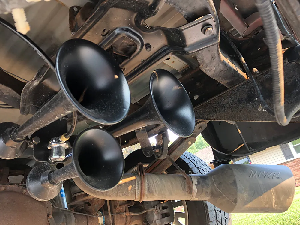 Three black train horns and MBRP exhaust tip installed on the rear undercarriage of a 2006 Ford F250